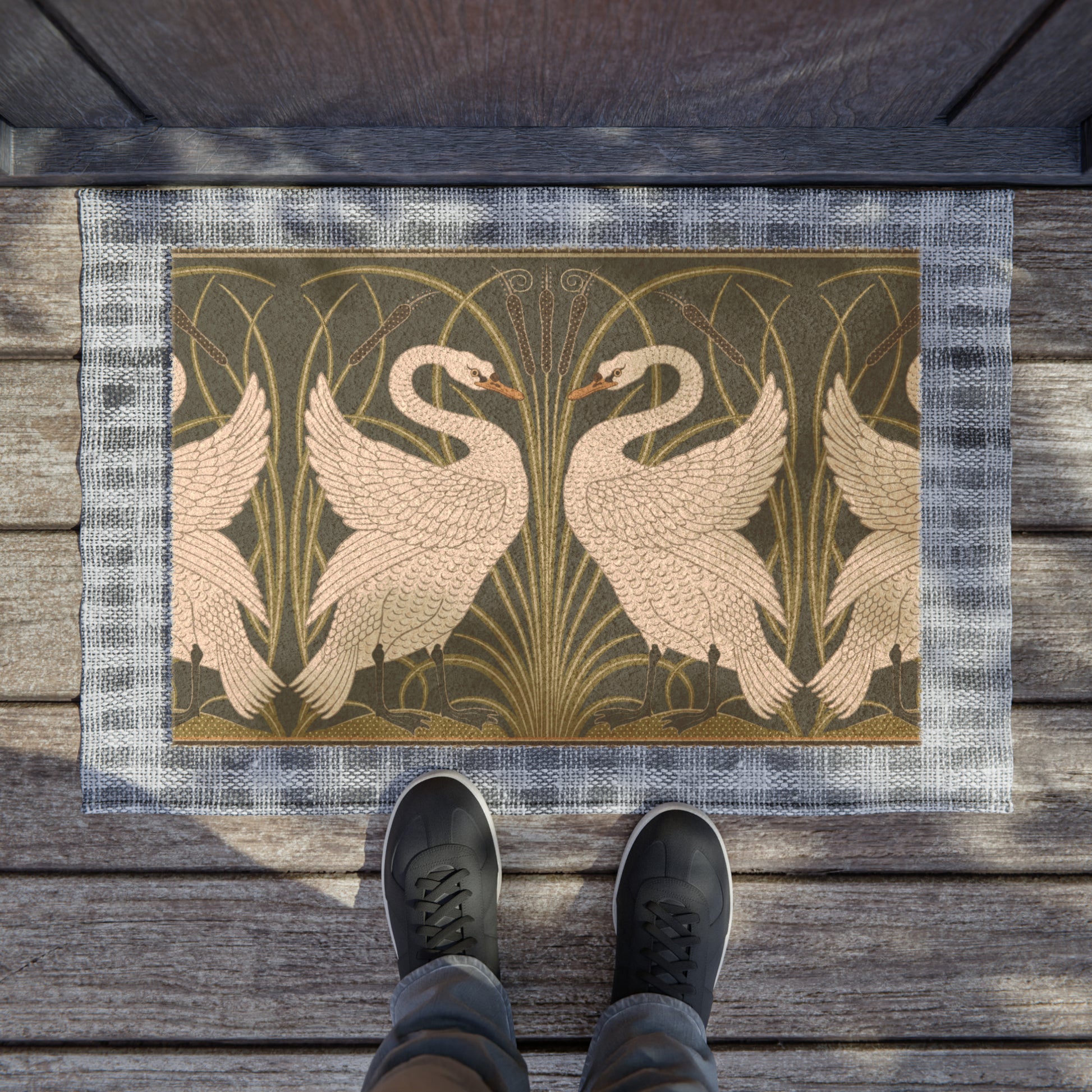 A rectangular doormat featuring a design of two white swans with a green and gold floral background, on a spruce green background.