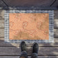 A rectangular doormat with a warm peach and tan floral pattern and a gray plaid border, shown on a wooden deck with a person's feet in dark sneakers standing at the bottom edge.