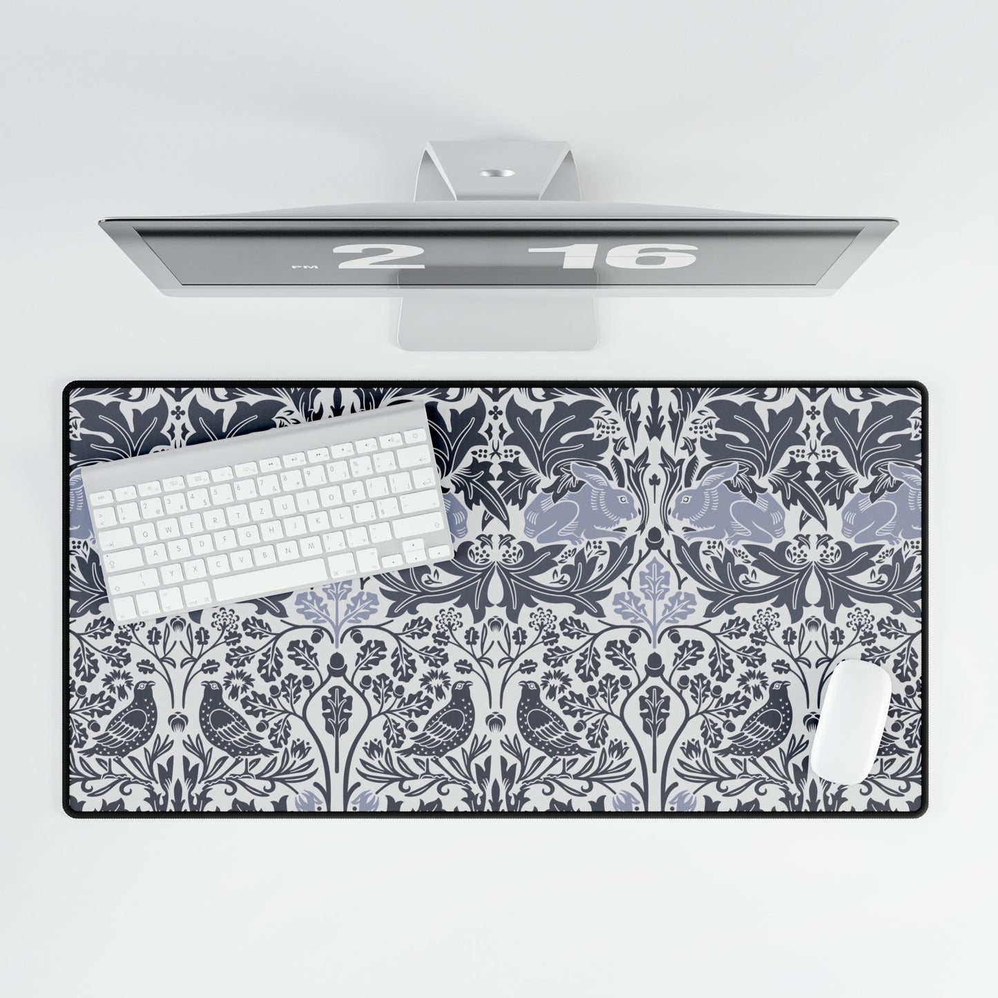 Desk setup with a decorative desk mat featuring a floral and bird pattern, keyboard, and computer monitor.