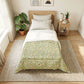 Bedroom with a bed featuring a green floral comforter, side table with lamp and books, and plants.