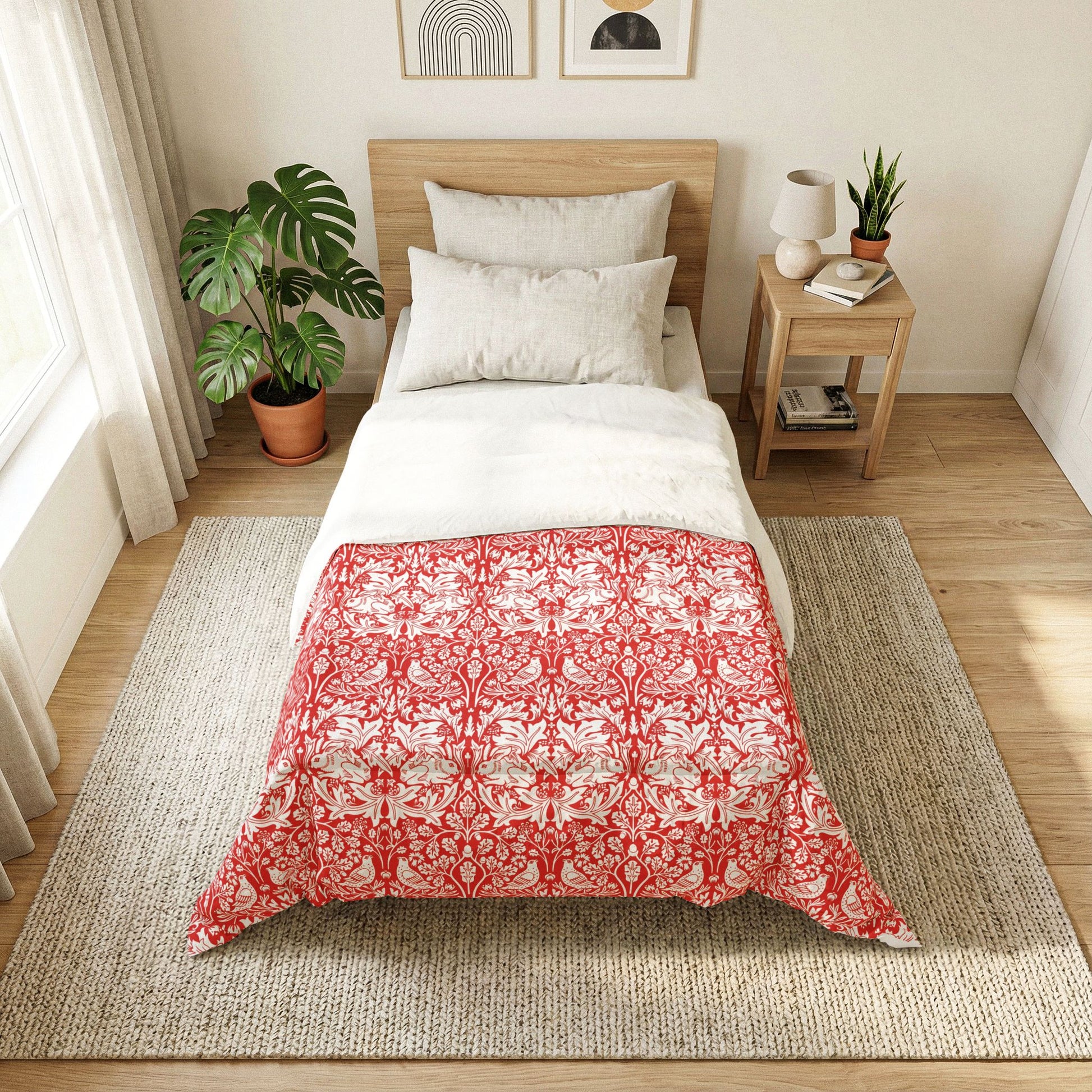 Bedroom with a bed featuring a red and white patterned comforter, side table with lamp and books, and plants.