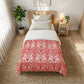 Bedroom with a bed covered in a red and white patterned comforter, nightstand, and plant.