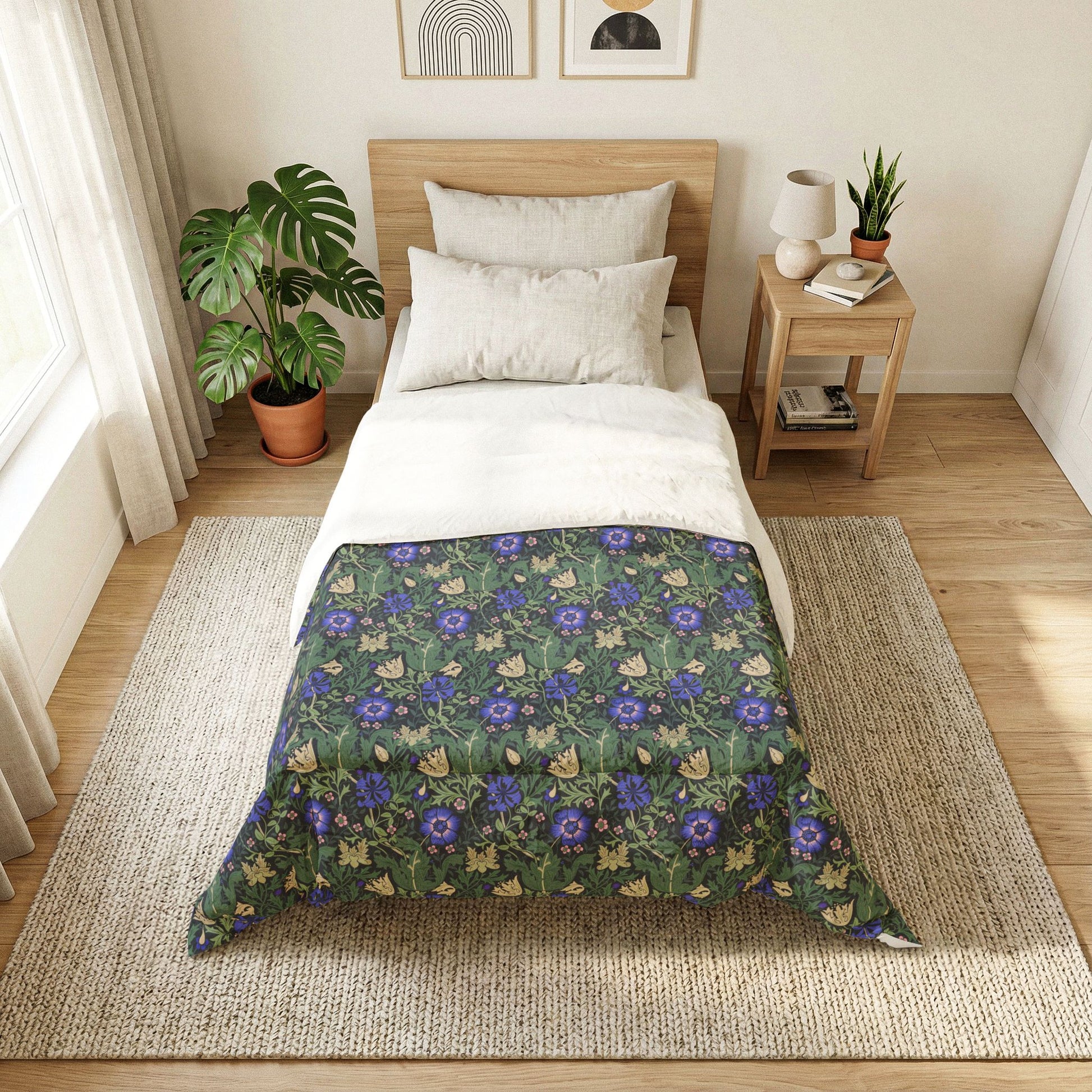 A neatly made bed in a bright, modern bedroom featuring a dark green floral comforter with blue and purple flowers and beige butterflies. The bed is styled with white sheets and pillows, set against a light wood headboard, with a matching wooden nightstand, a potted monstera plant, and a woven rug on a light wood floor.