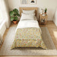 A neatly made single bed in a bright, minimalist bedroom. The bedding features a white duvet top and a cream-colored lower section with a colorful floral and botanical print in green, yellow, and pink.