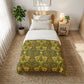 Bedroom with a bed covered in a green and yellow patterned duvet, nightstand, and plant.