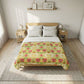 A floral patterned comforter or quilted blanket is styled on a wooden bed frame in a bright, modern bedroom. The pattern features red poppies and green leaves on a yellow and white background.