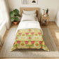 A neatly made bed in a bright, modern bedroom featuring a patterned comforter. The comforter has a light beige background with a repeating green leaf and red floral motif.