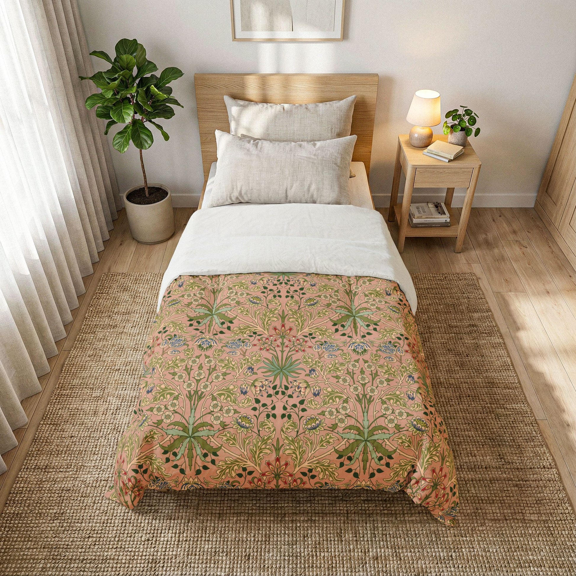 A neatly made bed in a bright bedroom setting, featuring a peach and green botanical patterned comforter with white pillows and a white top sheet. The bed is styled with a light wood headboard, a matching wooden nightstand with a lamp and small plant, and a large woven rug on a light wood floor.