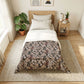 A neatly made bed in a bright, modern bedroom. The bedding set features a dark charcoal gray base with an intricate vintage floral and leaf pattern in beige, muted pink, and brown, layered over crisp white sheets and pillows.