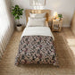 Bedroom with a bed featuring a floral-patterned comforter, nightstand, and plant.