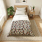 Bedroom with floral comforter on bed, side table with lamp and books, and plants.