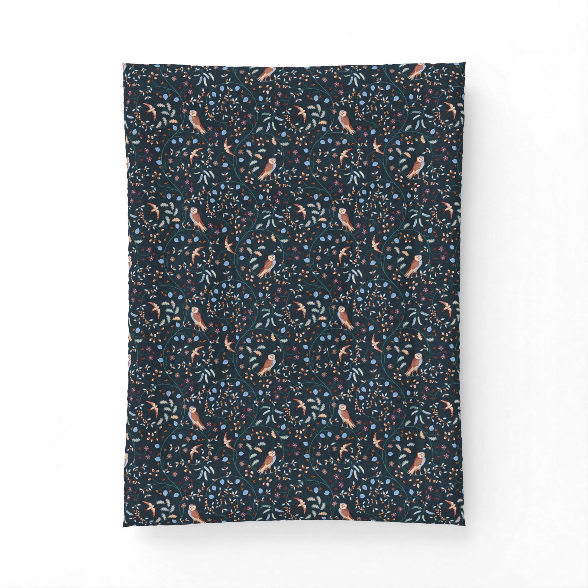 A rectangular fabric item, likely a pillowcase or small blanket, featuring a dense botanical and bird pattern on a dark navy background. The pattern includes light blue leaves, small orange and yellow flowers, and stylized birds in muted pink and brown tones.