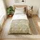 Bedroom with a bed featuring a green and white patterned comforter, nightstand with lamp and books, and plants.