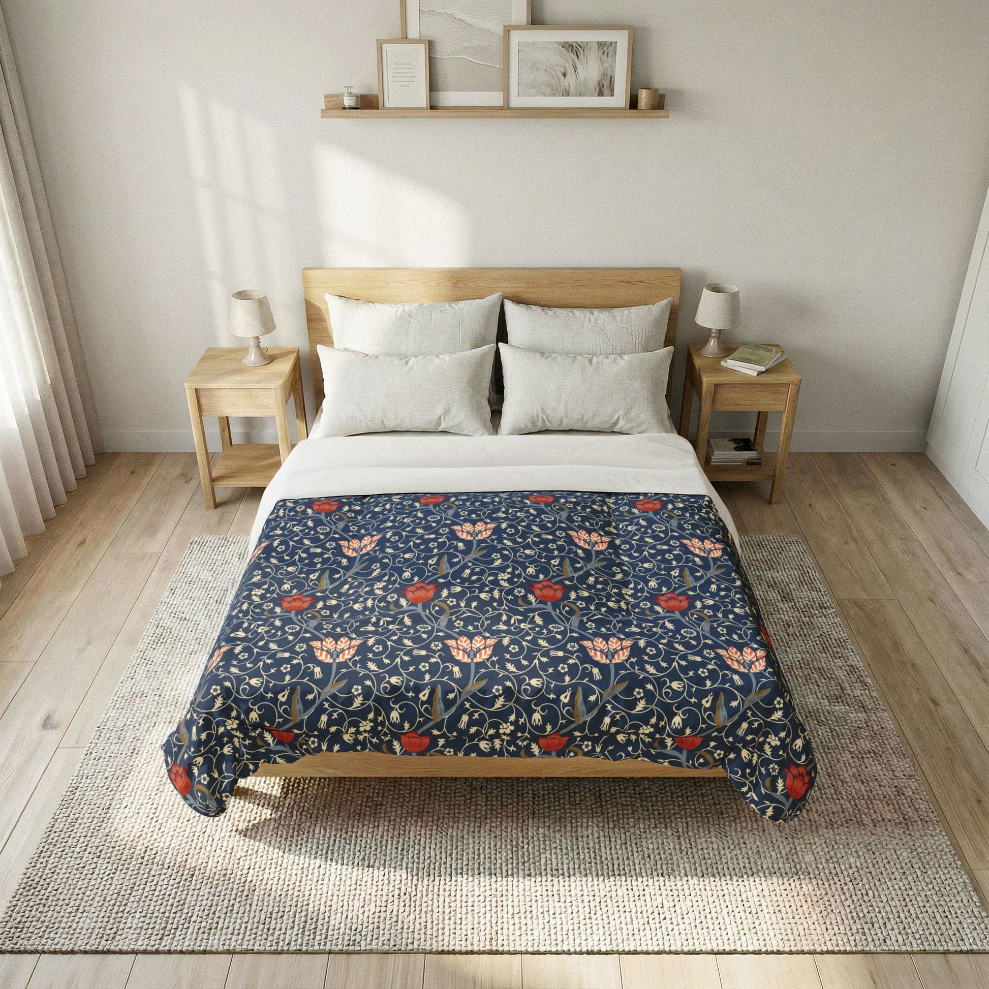 A neatly made bed in a bright bedroom, featuring a navy blue floral quilt with red and peach flowers, white pillows and top sheet, a light wood bed frame, two matching nightstands, and a woven rug.