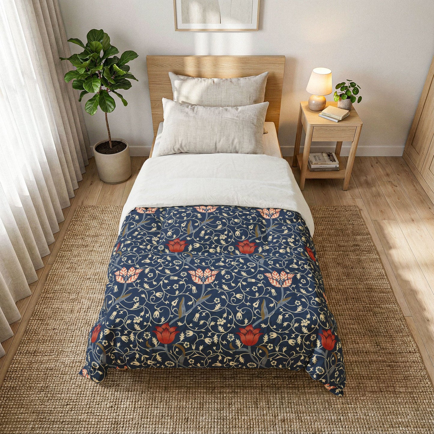A single bed styled in a bright, modern bedroom, featuring a navy blue comforter with a red and pink floral pattern, layered over white sheets and pillows. The bed is set on a woven jute rug next to a wooden nightstand with a lamp and a potted plant.