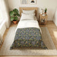 Bedroom with floral-patterned comforter on a bed, side table with lamp and books, and plants.