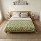 Bedroom with a bed featuring a green floral patterned duvet cover, two nightstands with lamps, and framed pictures on the wall.