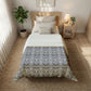 Bedroom with a bed covered by a patterned quilt, nightstand, and plants.