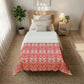 Bedroom with a bed covered in a red and white patterned comforter, nightstand, and plant.