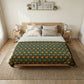 A neatly made bed in a bright, minimalist bedroom, featuring a dark green floral patterned comforter with orange flowers and a white sheet, set against a light wood bed frame.