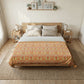 A neatly made bed in a bright, minimalist bedroom, featuring a patterned orange and yellow damask-style comforter over a white sheet, set on a light wood platform bed frame with neutral-toned pillows.