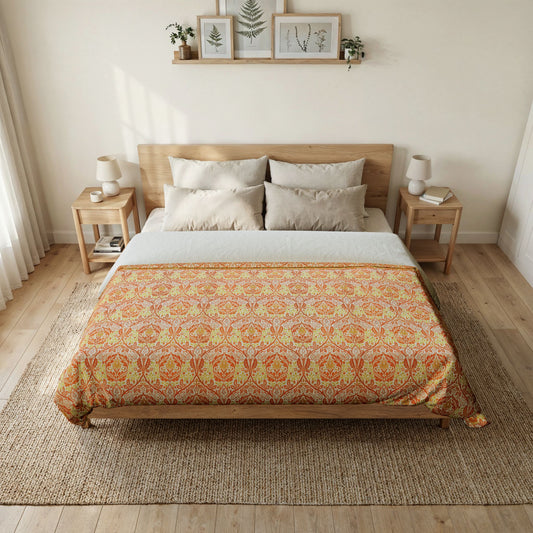 A neatly made bed in a bright, minimalist bedroom, featuring a patterned orange and yellow damask-style comforter over a white sheet, set on a light wood platform bed frame with neutral-toned pillows.