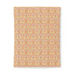 A rectangular fabric item, likely a towel or blanket, featuring an intricate repeating damask pattern in warm tones of orange, yellow, and soft pink on a light beige background.