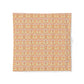A square fabric napkin or placemat featuring an intricate repeating damask pattern in warm tones of orange, yellow, and soft pink on a white background.