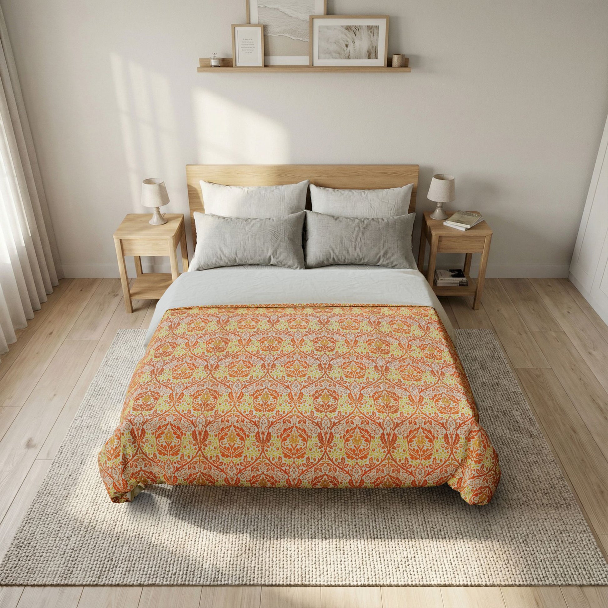 A bed dressed in a patterned orange and yellow damask-style comforter or quilt, styled in a bright, modern bedroom with light wood furniture, neutral walls, and a textured rug.