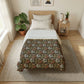 A neatly made bed in a bright, modern bedroom. The bedding set features a dark brown floral patterned comforter with white and orange accents, layered over white sheets and pillows, on a light wood bed frame.