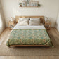 A neatly made bed in a bright, minimalist bedroom, featuring a green and beige floral patterned comforter, white sheets, and a light wood bed frame.