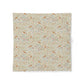 A square fabric napkin or small table linen featuring a dense vintage-style floral and bird pattern on a warm cream background, displayed flat against a white background.