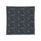 A square fabric item, likely a napkin or small tablecloth, featuring a dense all-over pattern of small birds, leaves, and berries on a dark navy blue background. The birds are a muted peach-pink color, while the foliage and berries are in shades of blue and green.