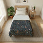 A neatly made bed in a bright, modern bedroom featuring a dark navy blue patterned comforter with a detailed bird and floral design, styled with white sheets and pillows on a light wood bed frame.