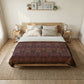 A bed dressed in a dark patterned throw blanket with a colorful bohemian-style floral design, styled in a bright, modern bedroom with a wooden bed frame, bedside tables, and neutral decor.