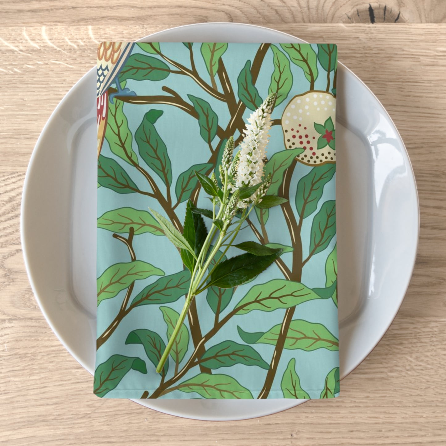 A blue cotton twill napkin with a floral design featuring birds and pomegranates is placed on a plate on a wooden table.