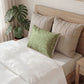 Bed with beige pillows and a green decorative pillow, next to a plant.