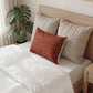 Bed with beige pillows and a red patterned pillow, next to a plant.