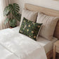Bed with beige pillows and a decorative green pillow featuring floral patterns, next to a plant.