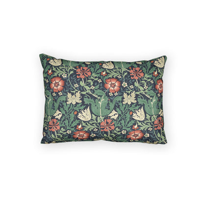 A rectangular decorative throw pillow featuring a dense floral and botanical pattern with red flowers, green leaves, and cream blossoms on a dark navy background, shown against a plain white studio backdrop.
