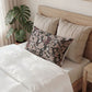 Bed with beige pillows and a purple accent pillow, next to a plant in a room.