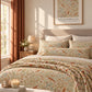 A beautifully styled bedroom featuring a bed dressed in a detailed botanical and bird patterned bedding set. The bedding has a cream background with intricate orange, green, and blue floral motifs and small birds.