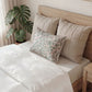 Bed with beige pillows and a decorative pillow with green leaf pattern, next to a plant.