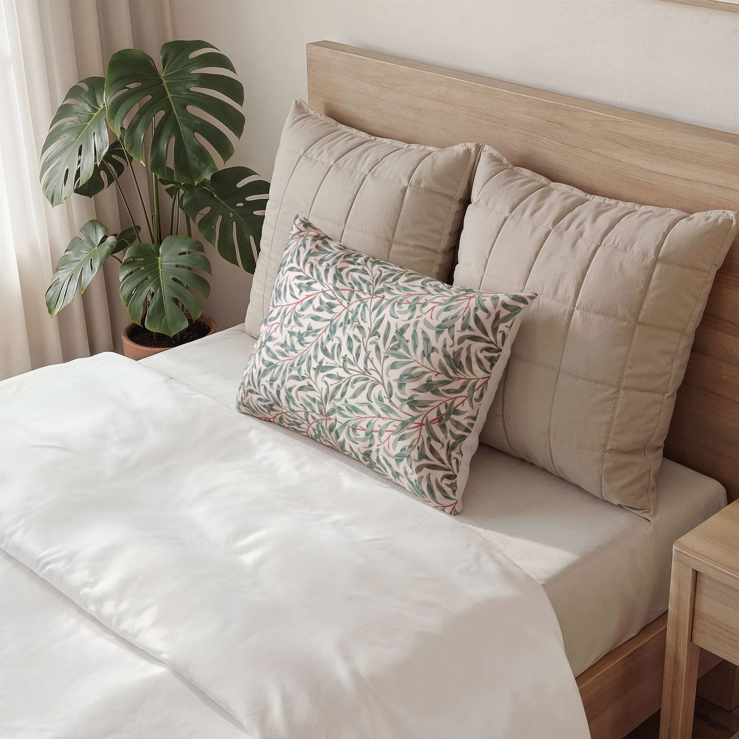 Bed with beige pillows and a decorative pillow with green leaf pattern, next to a plant.