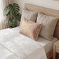Bed with beige pillows and a decorative pillow, next to a plant in a room.
