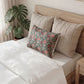 Neatly made bed with decorative pillows and a plant in the background