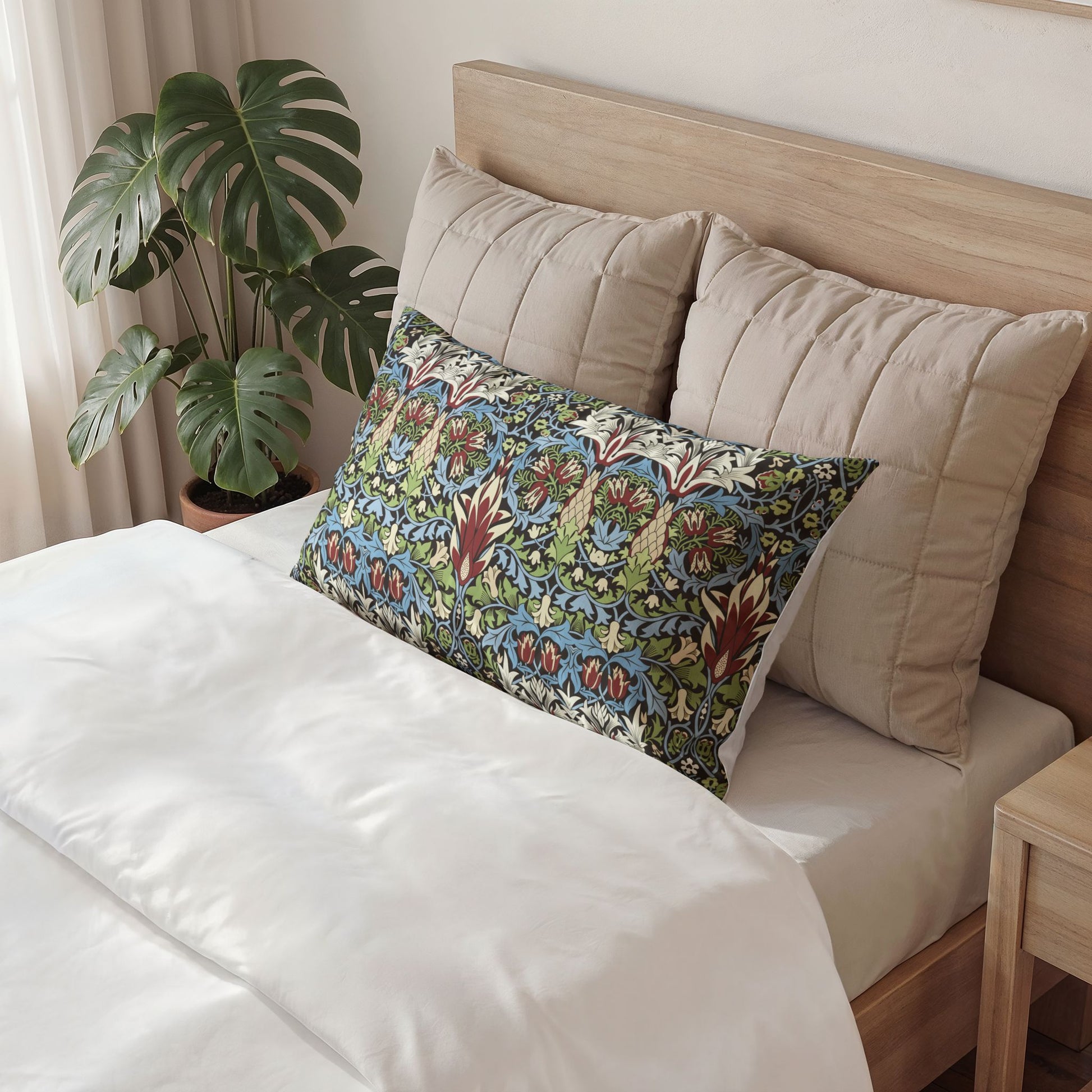 A decorative rectangular lumbar pillow with a colorful floral pattern in blue, green, and red, styled on a bed with beige pillows and white bedding in a bedroom setting.