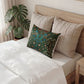 A decorative rectangular throw pillow with a detailed botanical pattern in dark green, teal, and orange, styled on a bed with beige quilted pillows and white bedding.