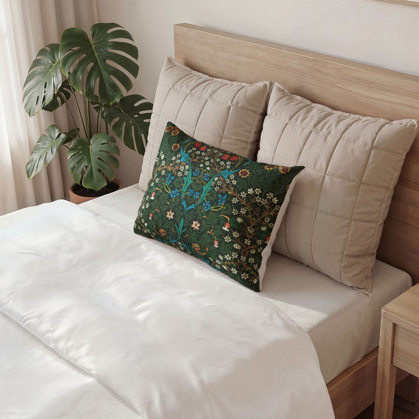 A decorative rectangular throw pillow with a detailed botanical pattern in dark green, teal, and orange, styled on a bed with beige quilted pillows and white bedding.