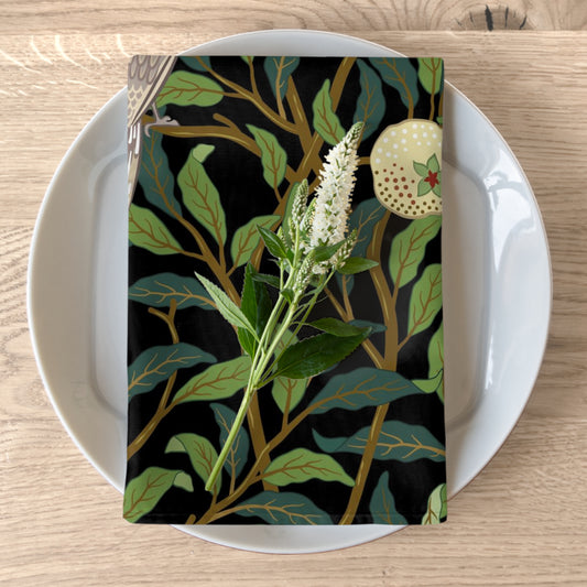 A cotton twill napkin with a floral design, featuring birds and pomegranates, laid on a plate next to a fork and a piece of bread.